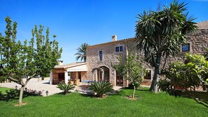 Une maison en pierre dotée d’un patio, entourée d’une végétation luxuriante et de palmiers.