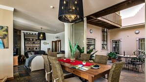 Un comedor con mesa de madera, sillas de mimbre y una araña.