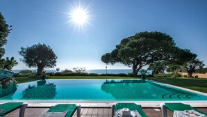 Un área junto a la piscina con sillones de descanso, una piscina azul cristalina y vistas al mar.