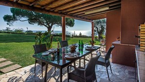 Un área de comedor al aire libre con una mesa de cristal, sillas de mimbre y vista al mar.