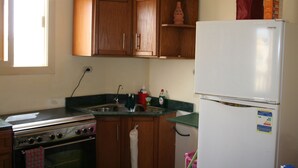 A compact kitchen with wooden cabinets, a stainless steel stove, a white refrigerator, and a window providing natural light.