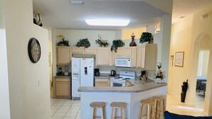 A modern kitchen with a central island, wooden stools, and a microwave above the stove.
