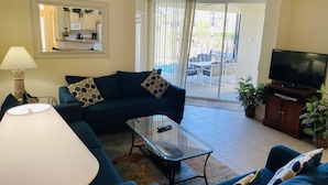 A living room with a sofa, a coffee table, a TV, and a sliding glass door leading to an outdoor patio.