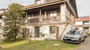 Ein zweistöckiges Haus mit Balkon, ein Auto vor der Tür und ein großer Baum im Garten.