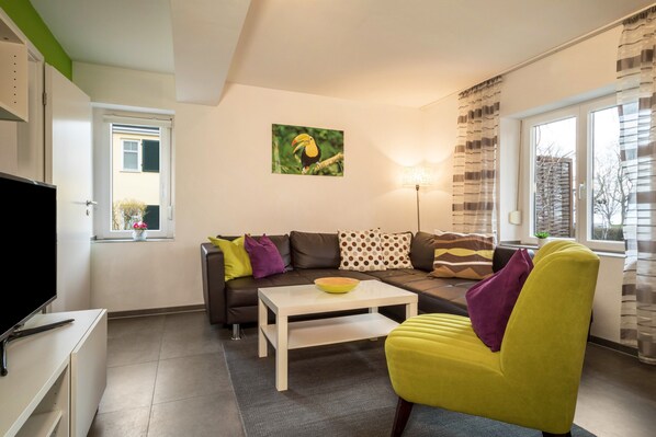 A modern living room with a sofa, armchair, coffee table, and a painting on the wall.