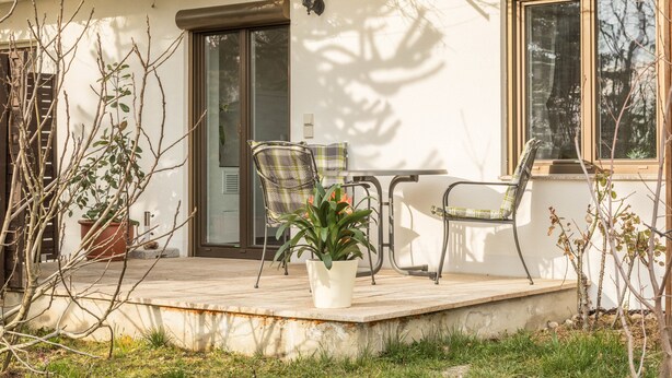 Eine Terrasse mit Tisch, Stühlen und einem Blumentopf, sowie einer Tür.