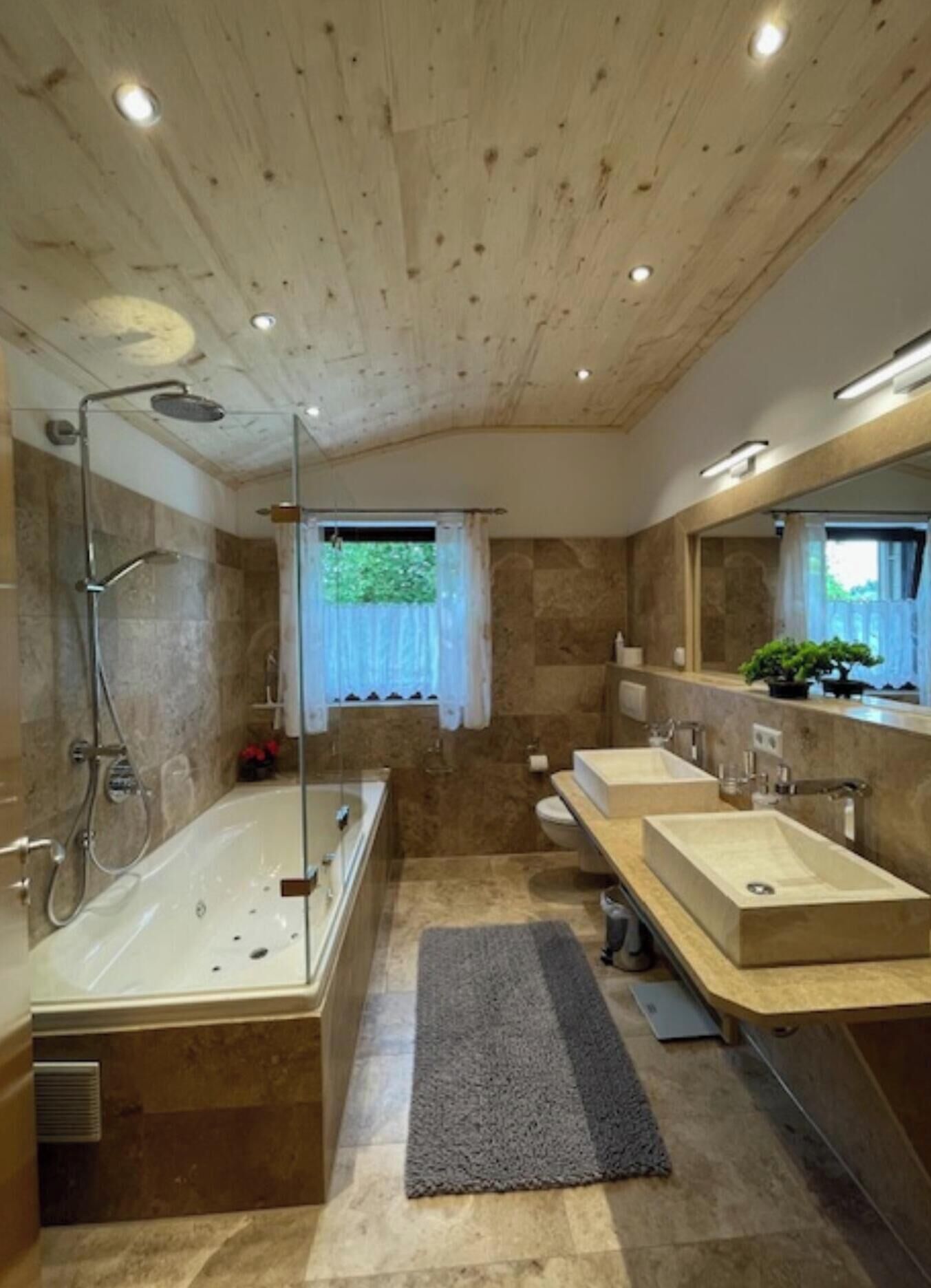 A modern bathroom with a wooden ceiling, a bathtub, a shower, and two sinks.