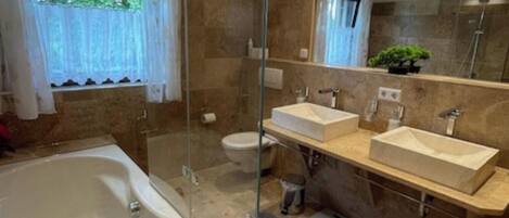 A modern bathroom with a glass-enclosed shower, a freestanding bathtub, and two sinks.