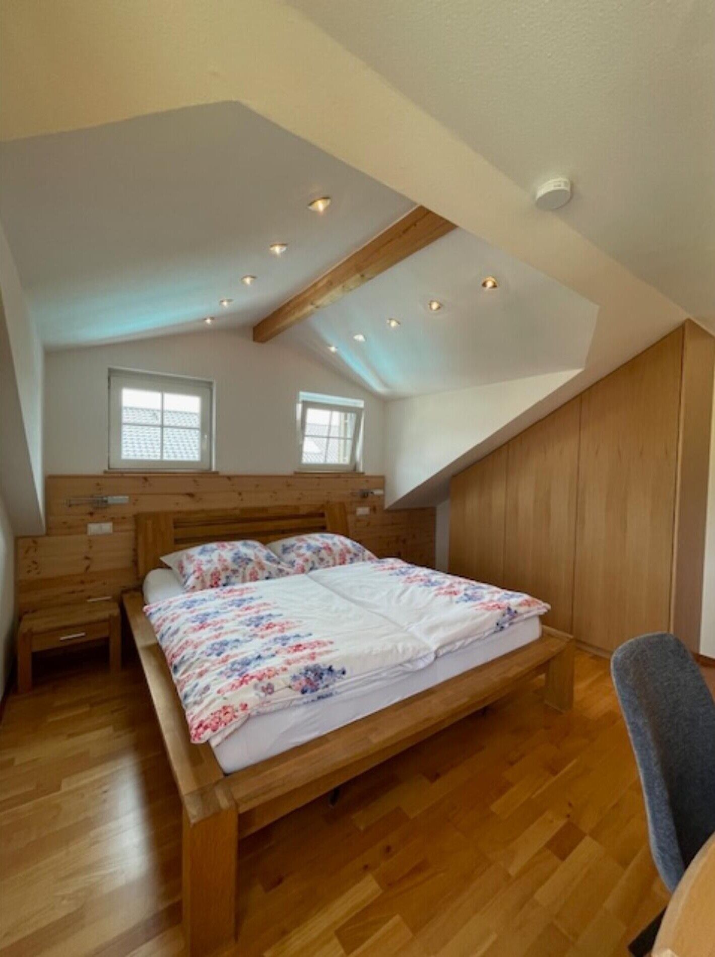Een slaapkamer met een houten bed, twee ramen en een schuine kap.