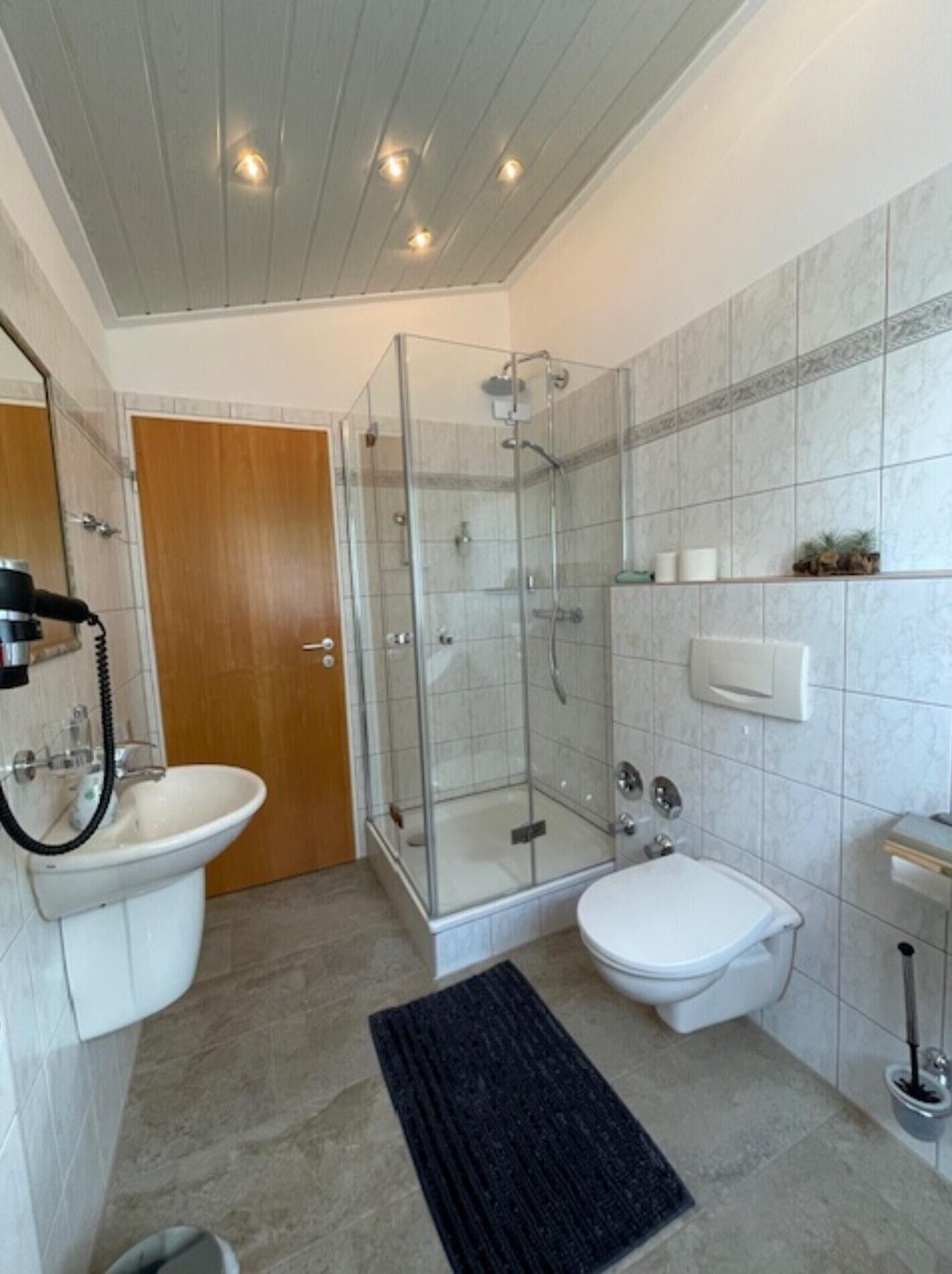 A bathroom with a glass-enclosed shower, a toilet, a sink, and a wooden door.
