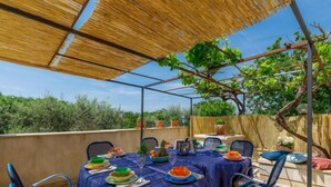Un espace extérieur aménagé pour les repas, avec une terrasse couverte, une table dressée pour quatre personnes et des chaises.