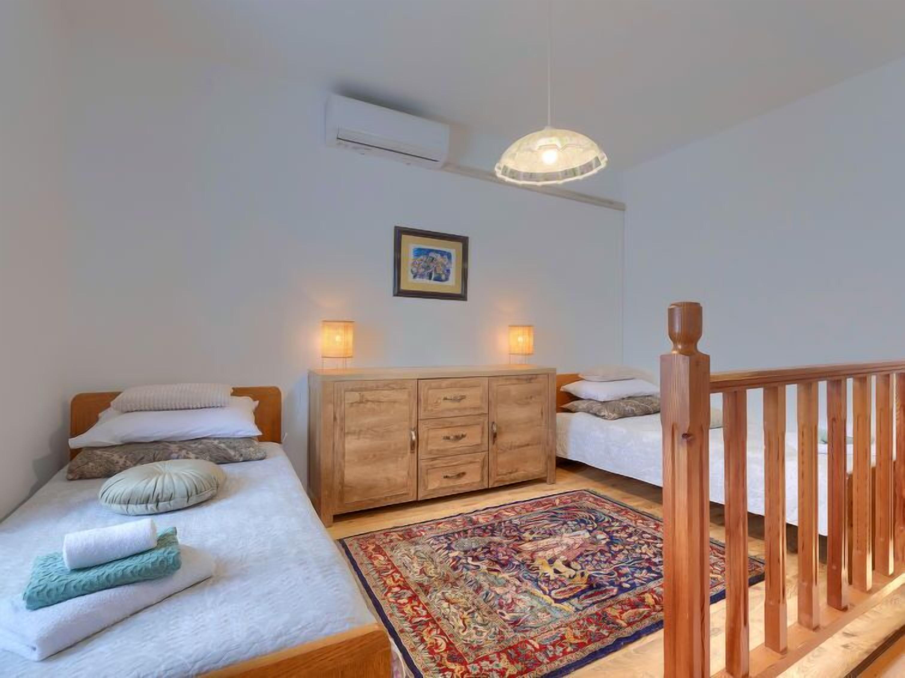A bedroom with two beds, a wooden wardrobe, a colorful rug, and a wooden railing.