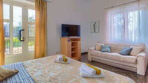 Une chambre d’hôtel avec un lit, un canapé, une télévision et un balcon avec des rideaux.