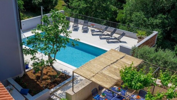 Un espace piscine aménagé sur le toit, avec des chaises longues, une table à manger et un petit jardin.