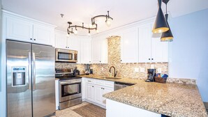 A modern kitchen with stainless steel appliances, granite countertops, and white cabinetry. - Right on the Beach - Pool - 1BR 1BA - King & Bunks (Santa Rosa Beach)