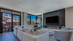 A modern living room with a large sofa, a fireplace, and a TV. - Ski-in/out, Best Views, Best Location at Snowmass Base Village | One Snowmass (Snowmass Village)