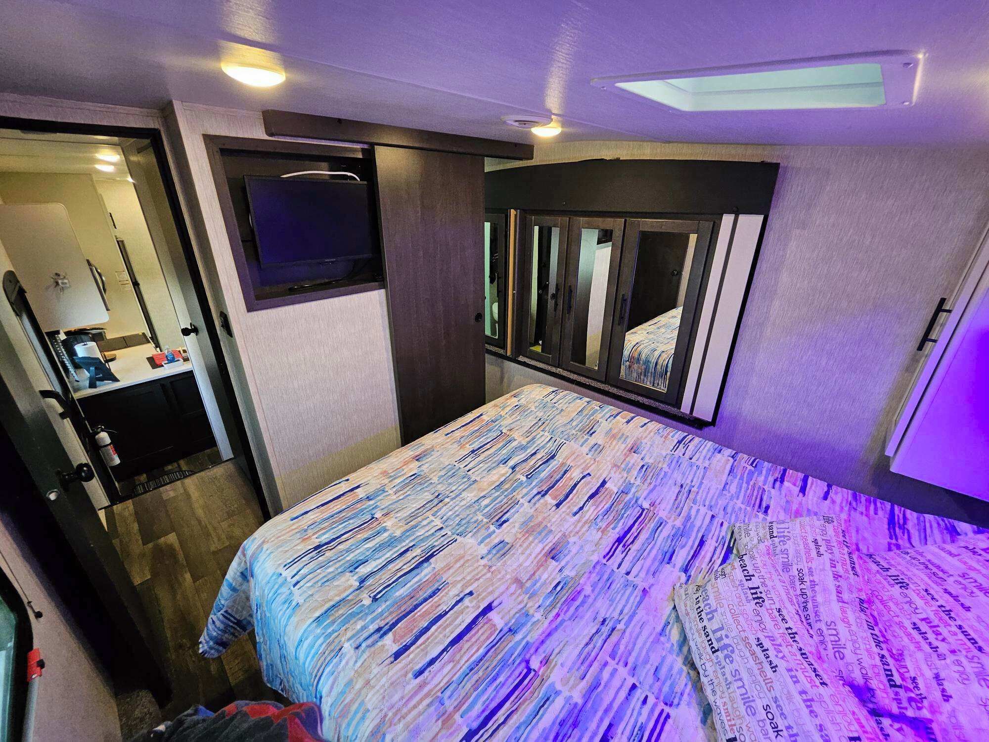 A bedroom with a bed, a mirror, a television, and a door leading to a bathroom.