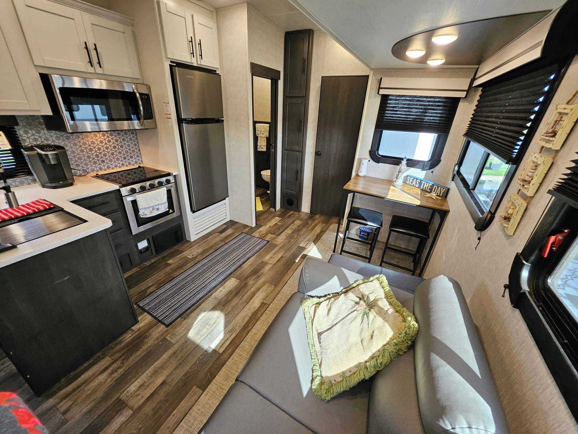A compact RV kitchen with a microwave, stove, refrigerator, and a small dining area with a table and bench.