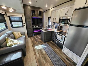 A compact RV kitchen with a refrigerator, stove, microwave, and a seating area with cushions. - RV9 | Family Beach Getaway -  Cruiser Aire (Gilchrist)