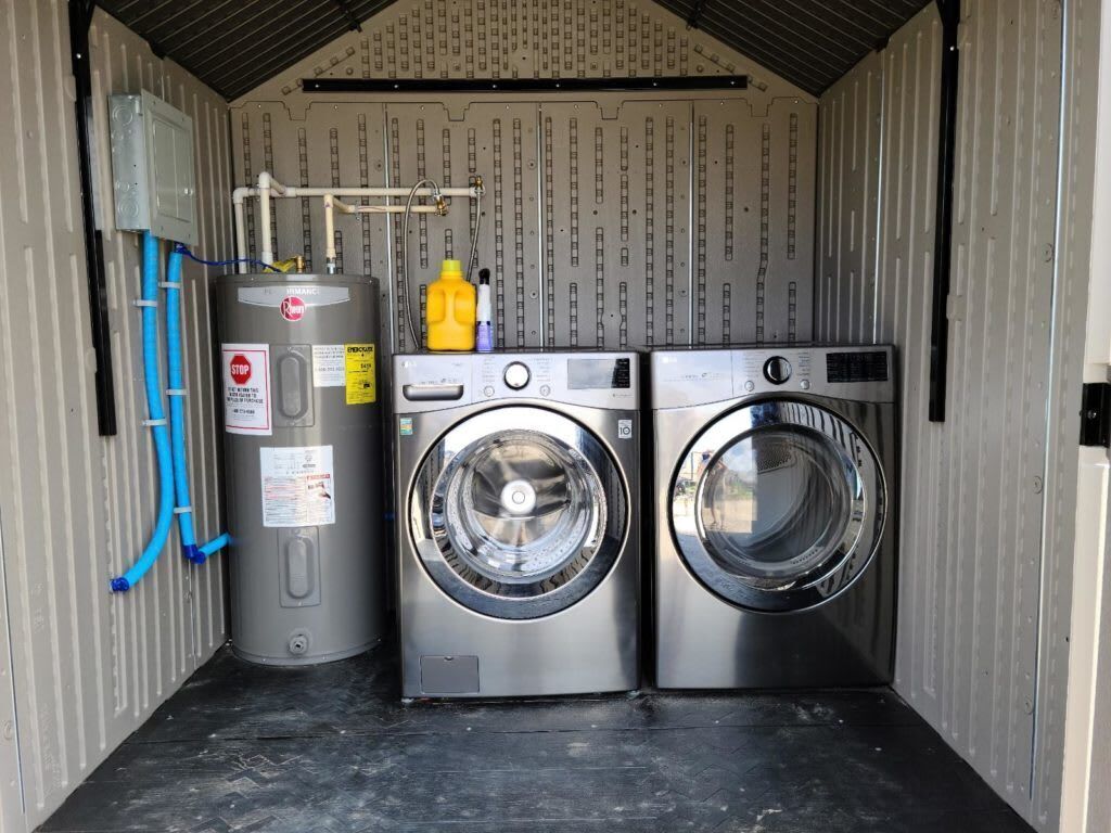 A compact laundry room with a water heater, two washing machines, and a hose.