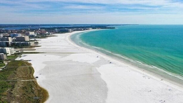 Une plage côtière avec une vaste étendue de sable, une mer bleue et limpide, et des bâtiments qui bordent le littoral.