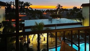 Une vue depuis un balcon donnant sur une piscine et sur un coucher de soleil sur l’océan.