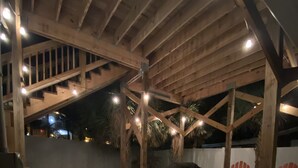 En udendørs terrasse med træbjælker, flisegulv og udendørs møbler, herunder sofaer og stole.
