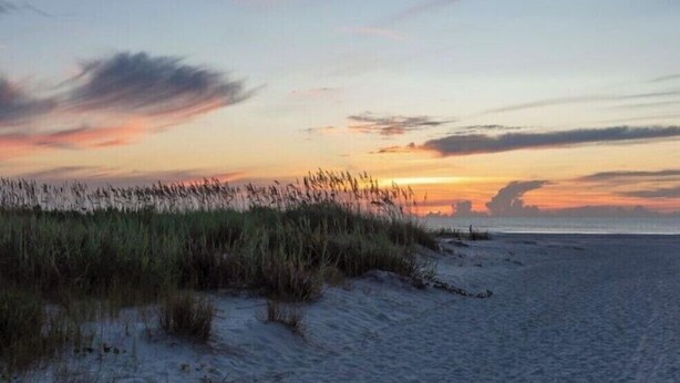 En strand med klitter og en solnedgang.
