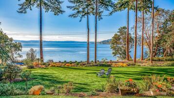 A well-maintained lawn with two Adirondack chairs facing a scenic view of a lake and tall trees.