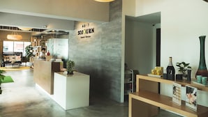 Uma área de recepção com uma placa indicando 'SOJOURN Guest House', um balcão de recepção e um mostrador com diversos itens.