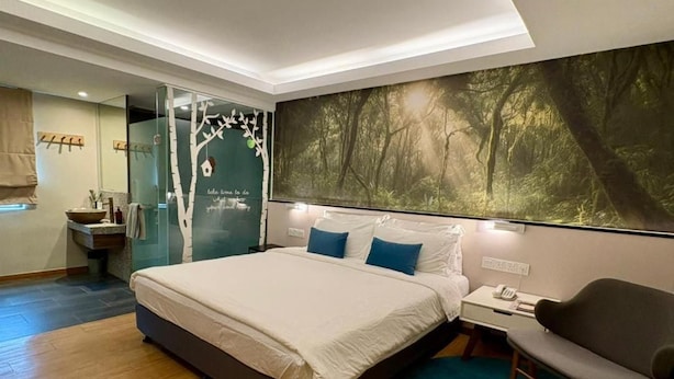 Quarto moderno com uma cama grande, mesa de cabeceira, cadeira e banheiro com box de vidro.