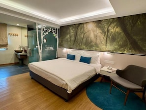 A modern bedroom with a large bed, a nightstand, a chair, and a bathroom with a glass shower enclosure. - Sojourn Guest House (Ampang)