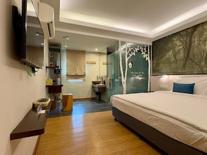 A modern hotel room with a large bed, a flat-screen TV mounted on the wall, a small bathroom with a sink and mirror, and a large window with a view of trees. - Sojourn Guest House (Ampang)