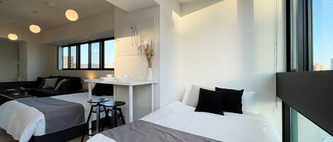 A modern hotel room with two beds, a small desk, and a large window.