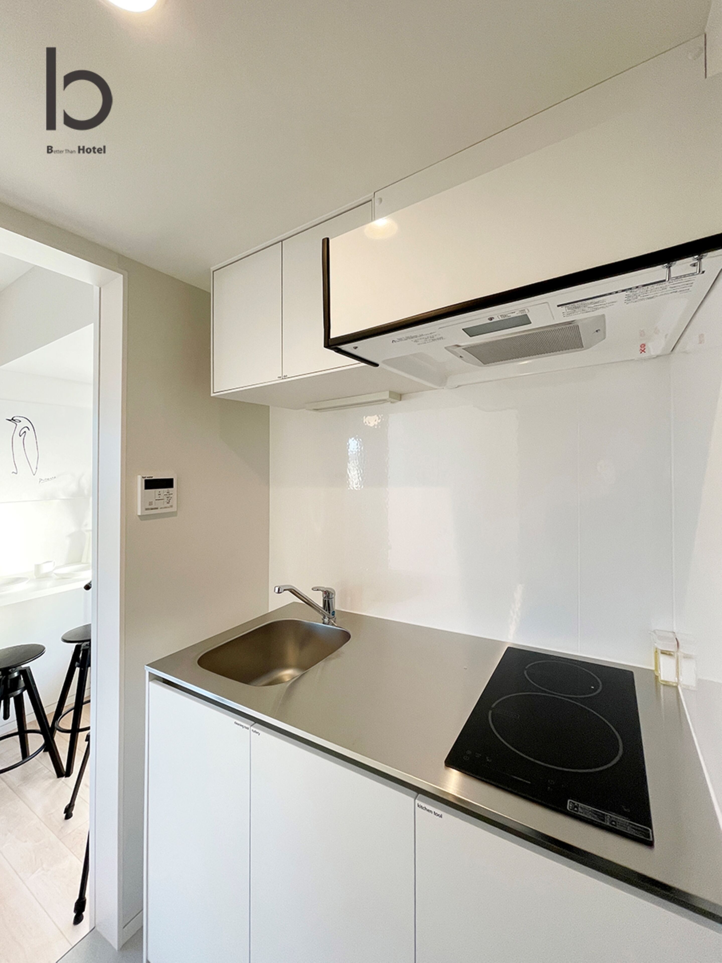 A modern kitchen with a stainless steel sink, a black induction cooktop, and white cabinetry.