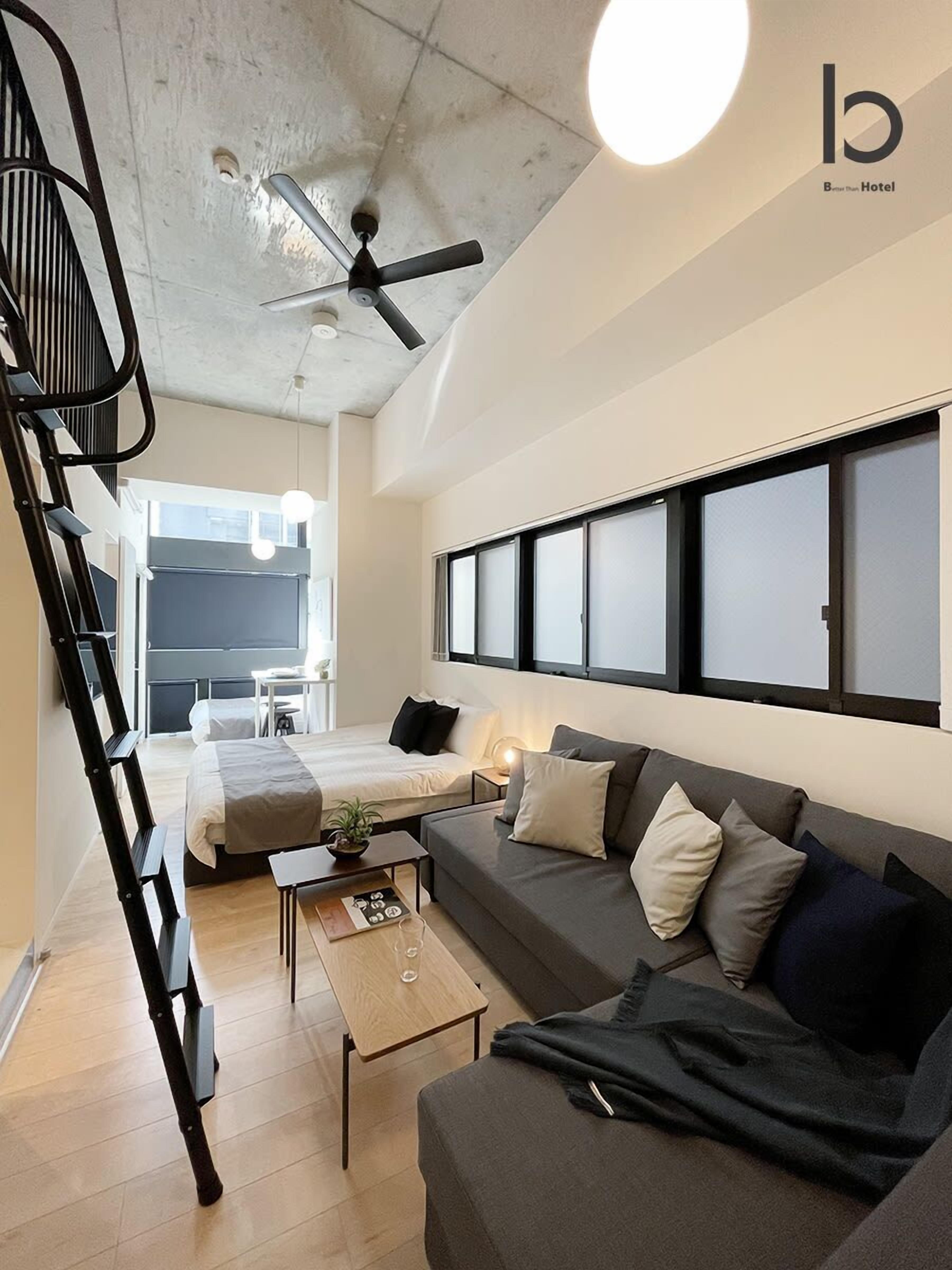 A modern hotel room with a loft bed, a sofa, a coffee table, and a ceiling fan.