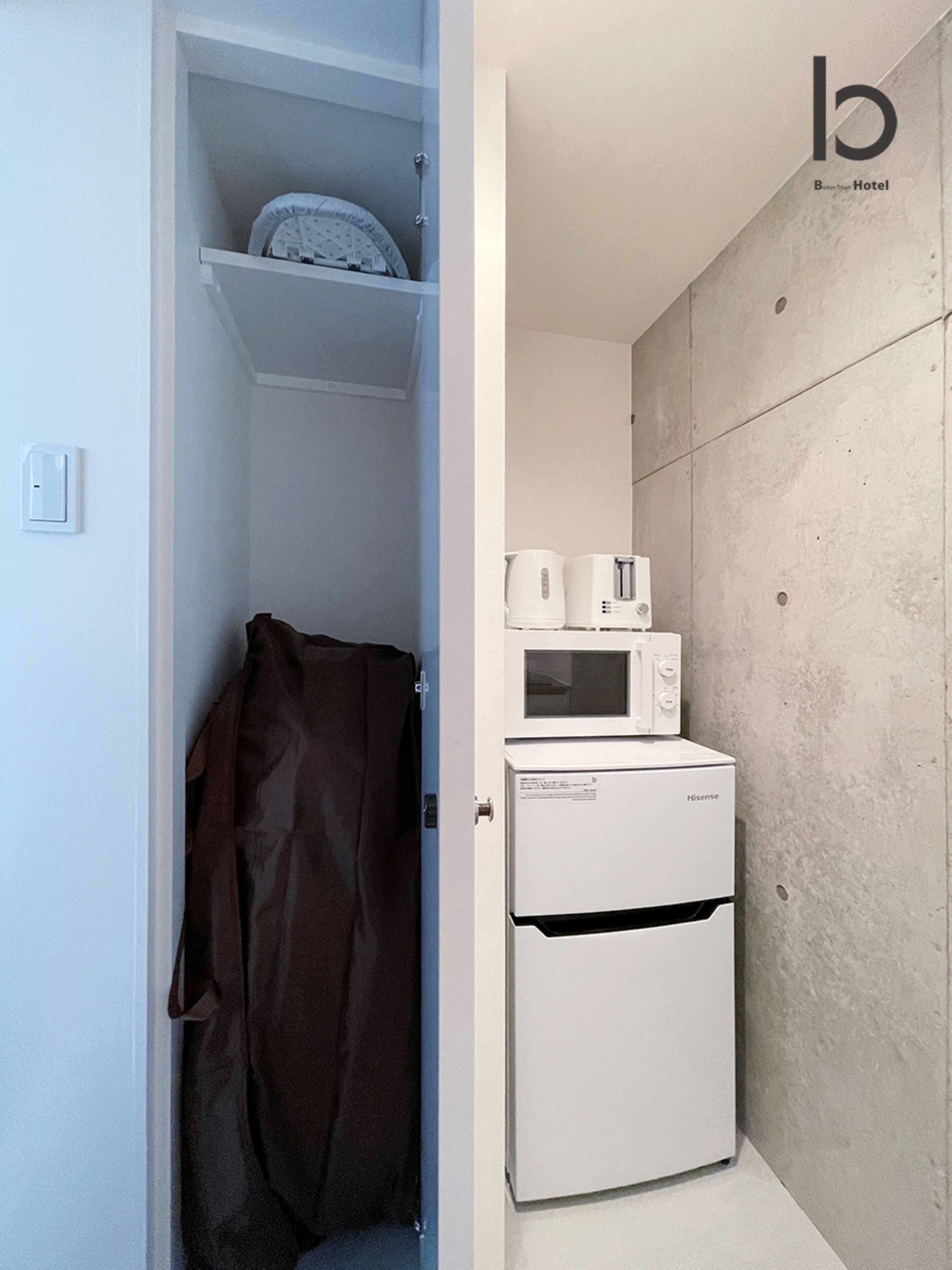 Een compacte kitchenette met een magnetron en een kleine koelkast. Een bruine handdoek is over de deur gehangen.