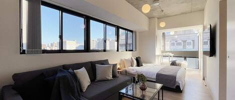A modern hotel room with a sofa, a bed, a small table, and a TV.