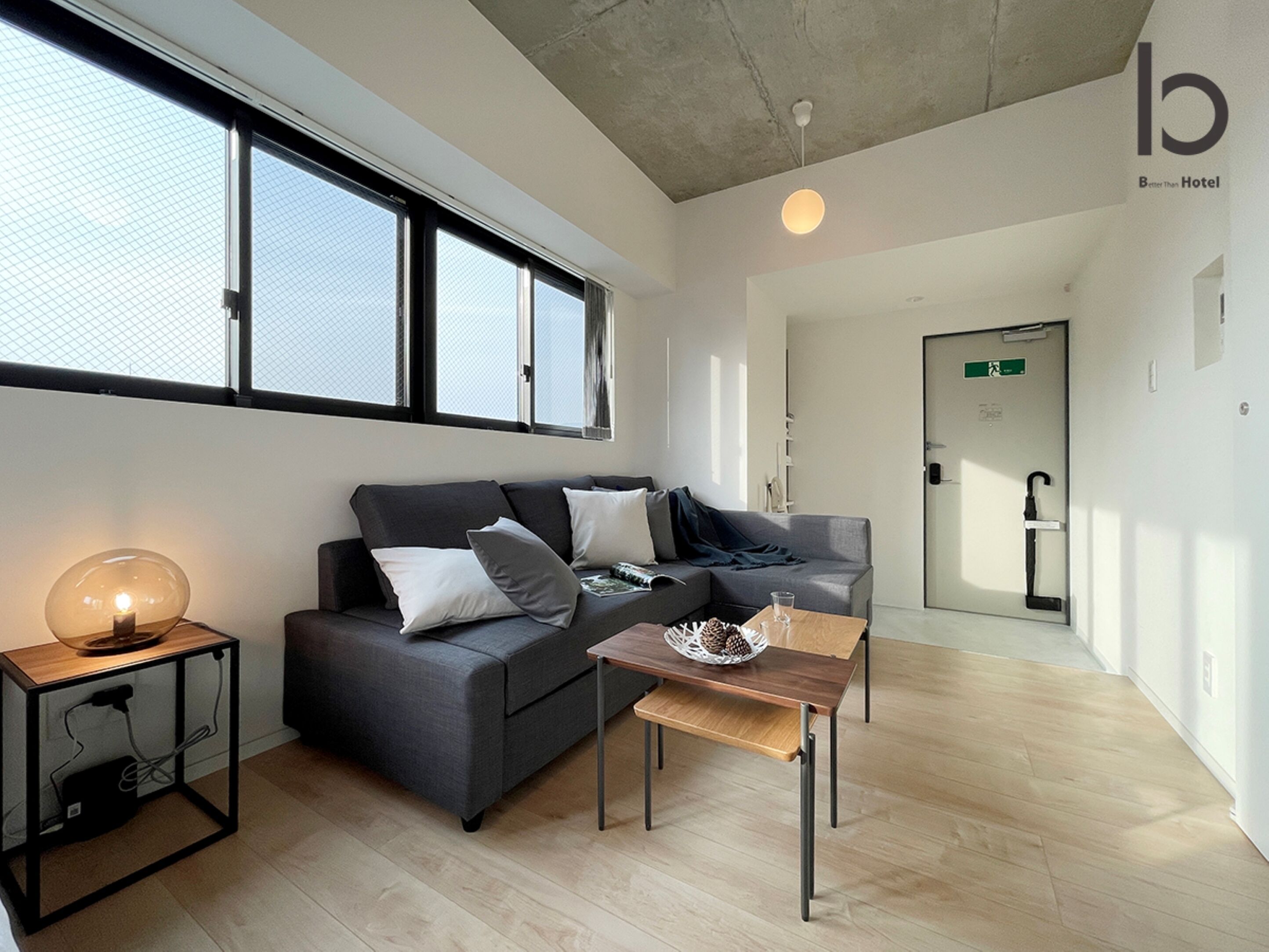 A modern hotel room with a grey sofa, a small wooden table, and a floor lamp.