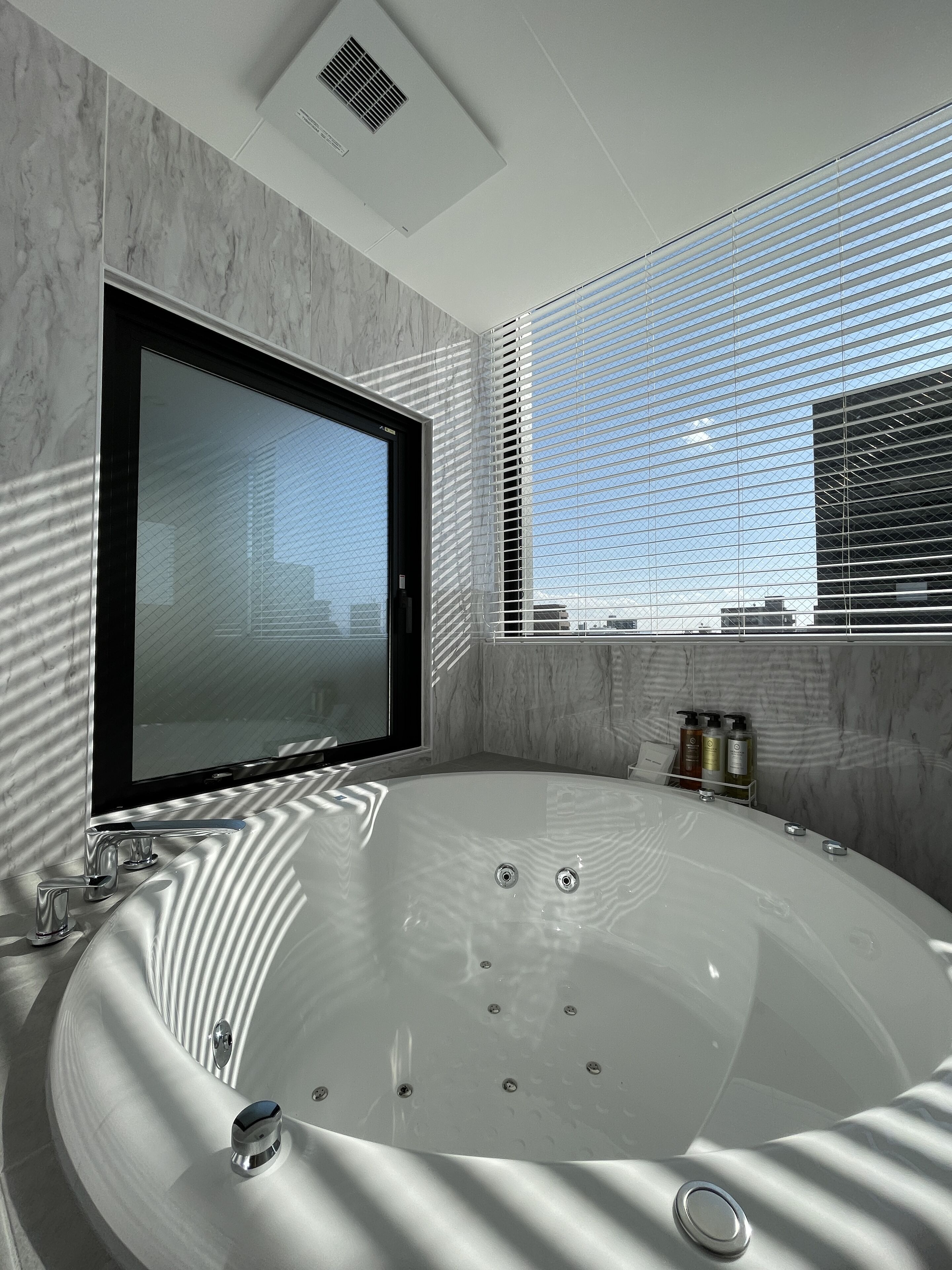 Ein modernes Badezimmer mit einer großen Badewanne, einem Fenster mit Jalousien und einem Spiegel.