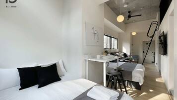 A modern hotel room with a bed, a desk, and a kitchenette.