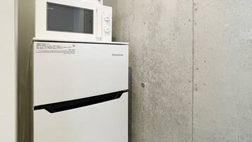 Un refrigerador Hisense blanco y compacto con un microondas encima, colocado contra una pared lisa y con textura.