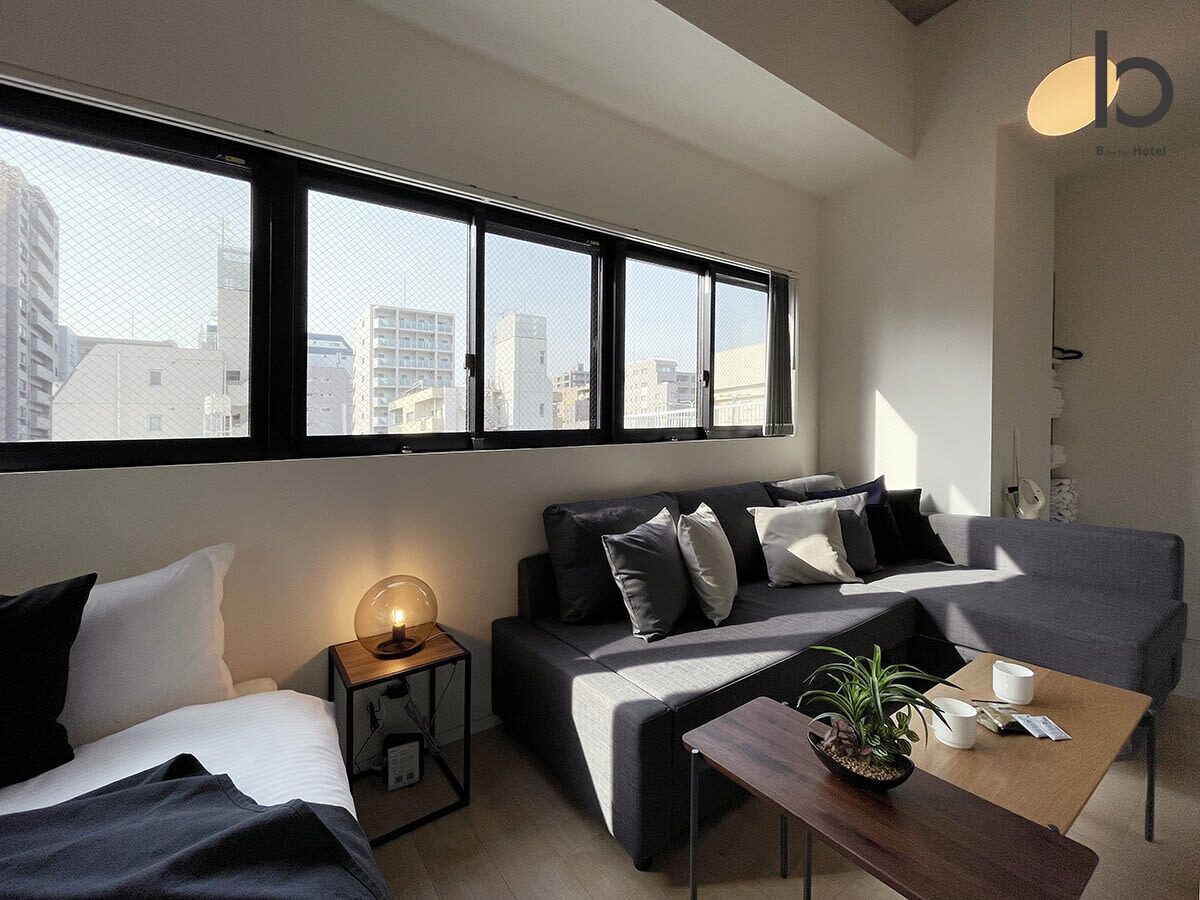 A modern hotel room with a sofa, a small table with a plant, and a bedside lamp.