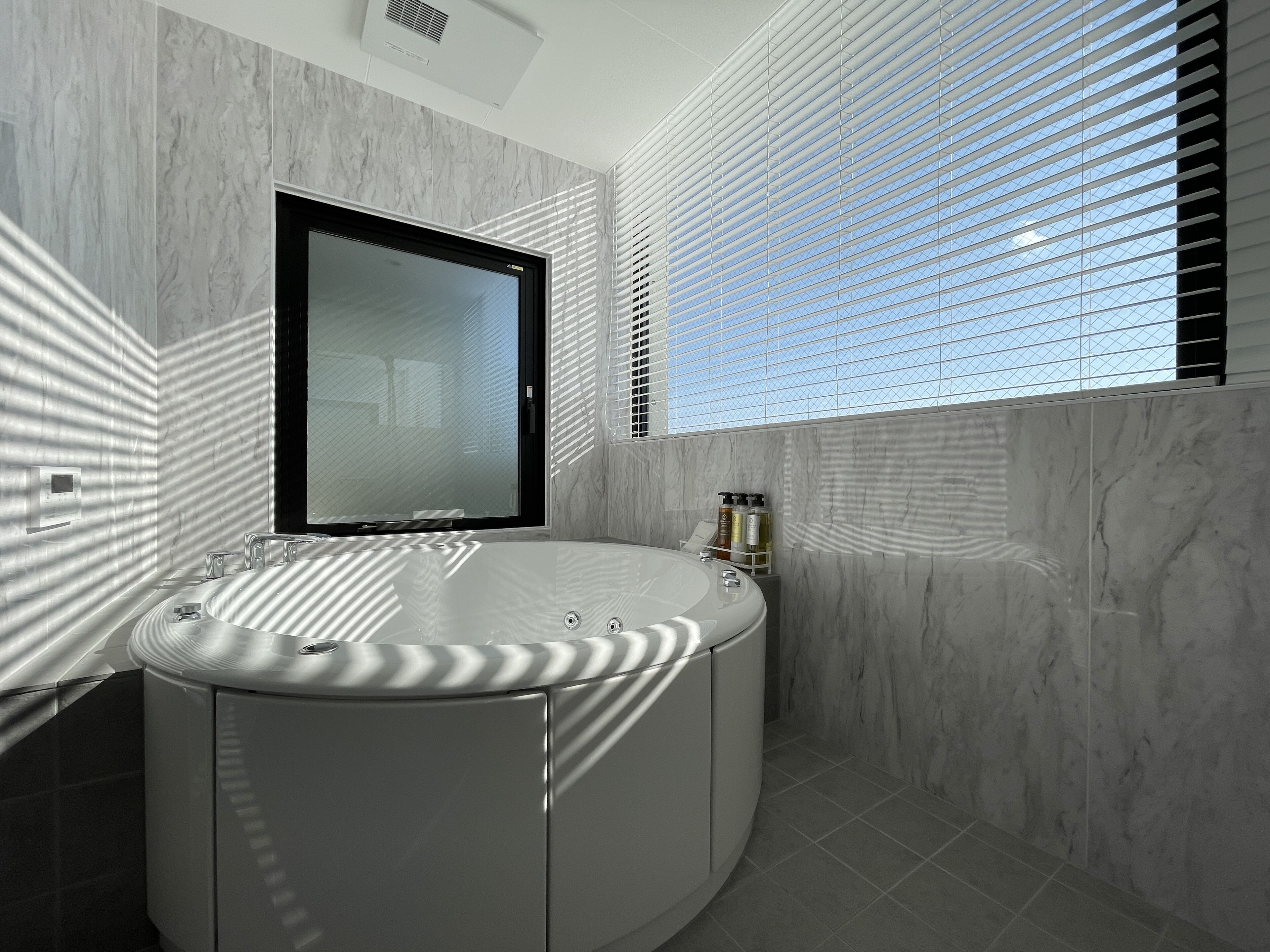 A modern bathroom with a freestanding bathtub, a large mirror, and a window with blinds.