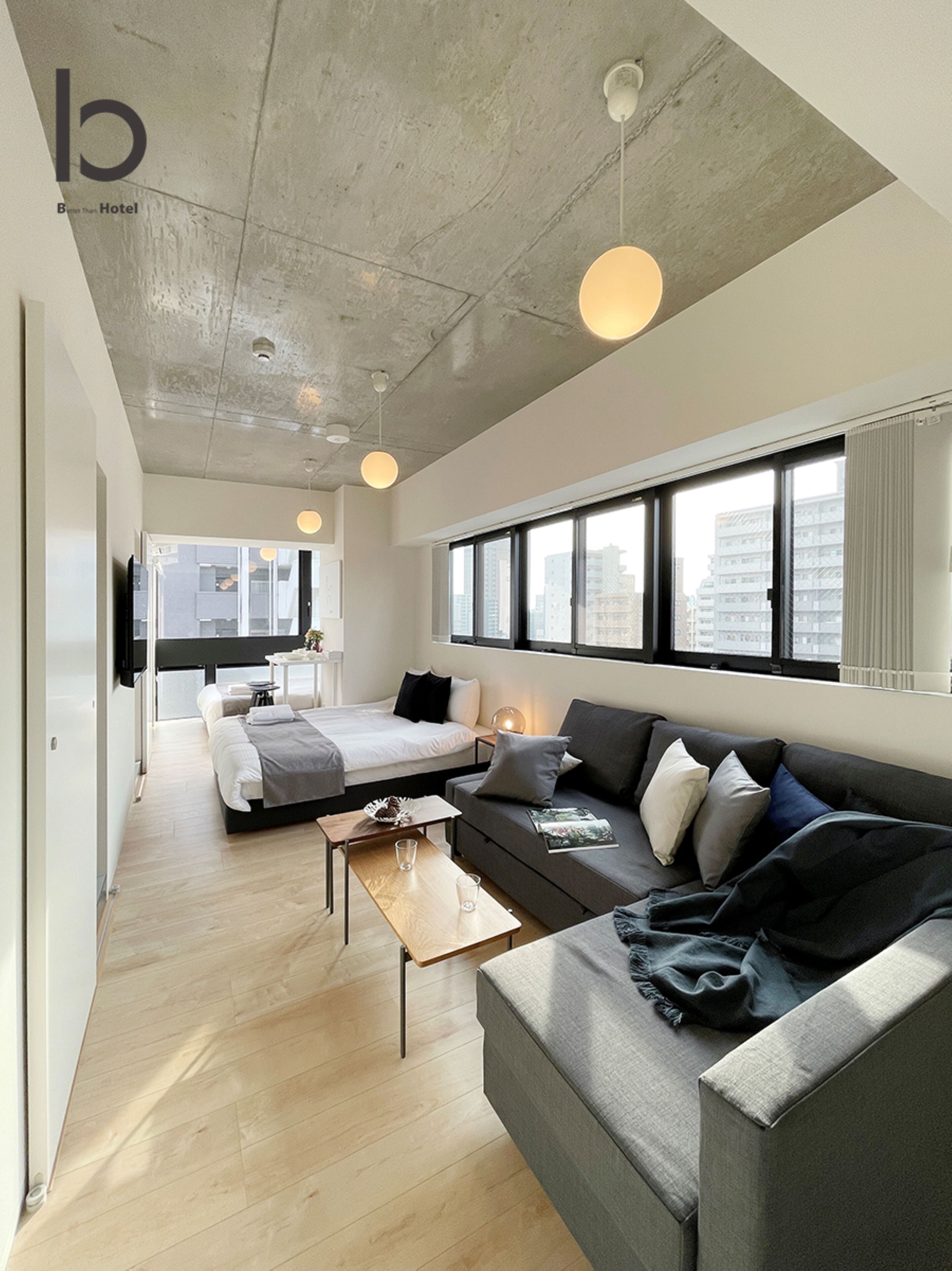 A modern hotel room with a large bed, a sofa, a coffee table, and a view of the city through large windows.