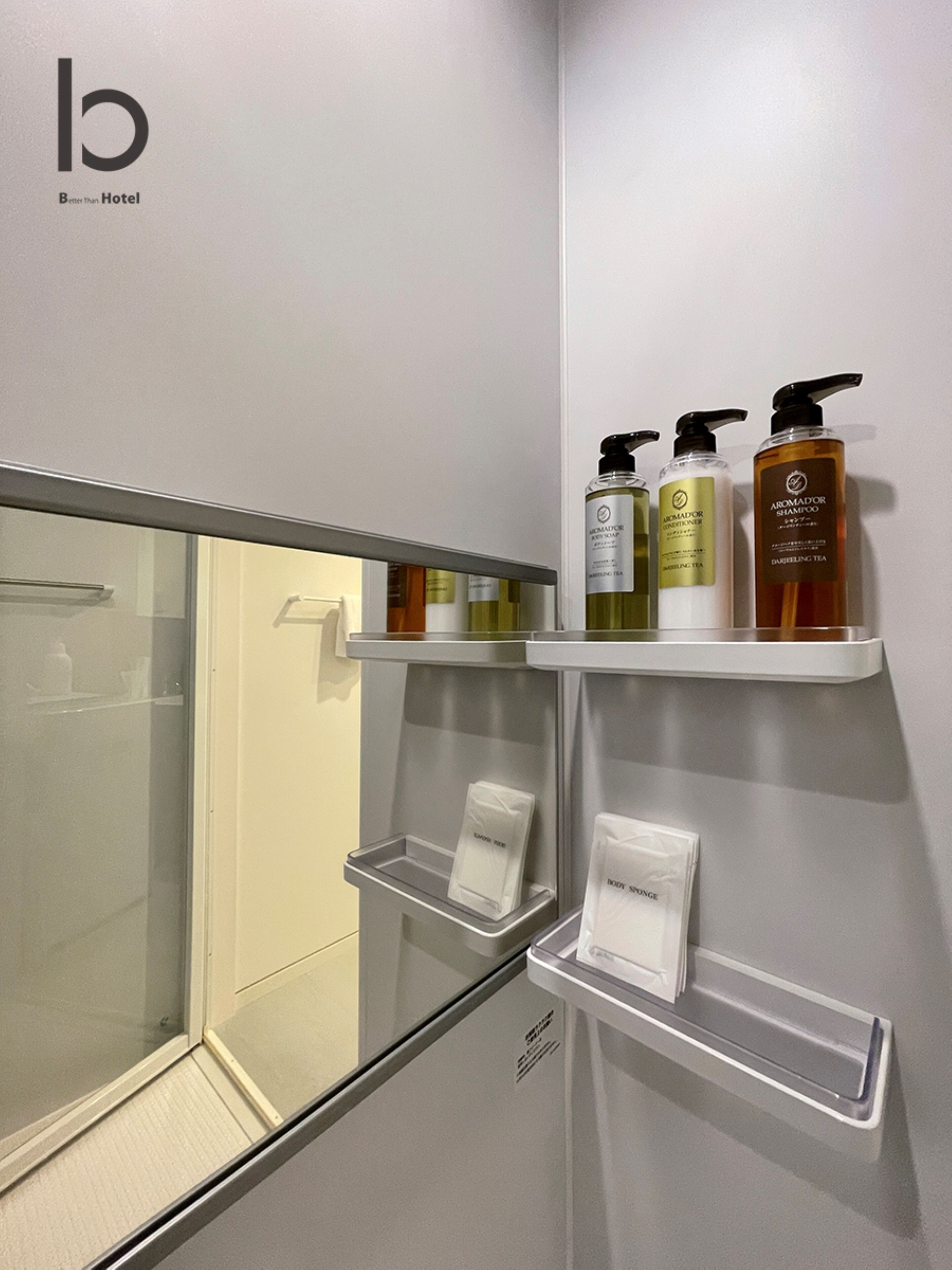 Baño de hotel con cabina de ducha de vidrio, repisas con artículos de aseo y un logotipo visible.