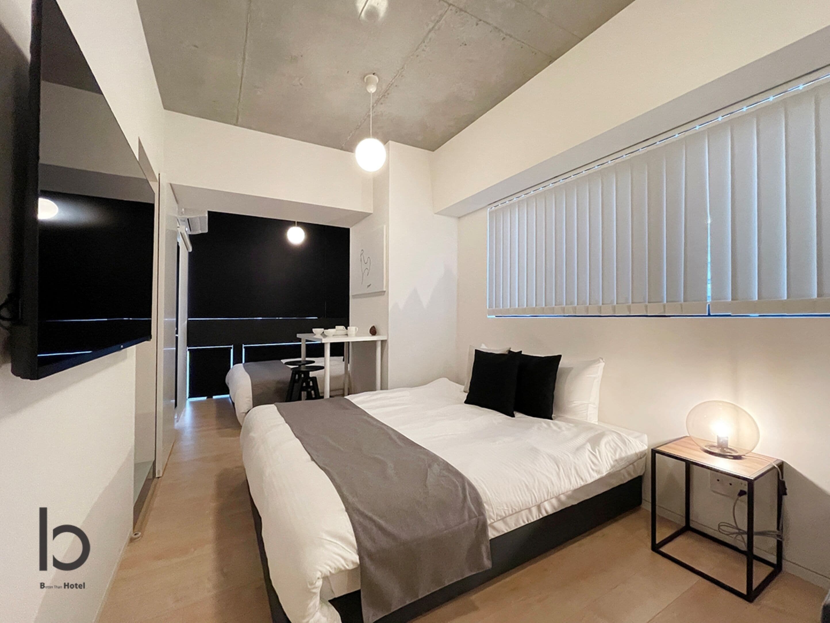 A modern hotel room with a large bed, a desk, a TV, and a window with blinds.