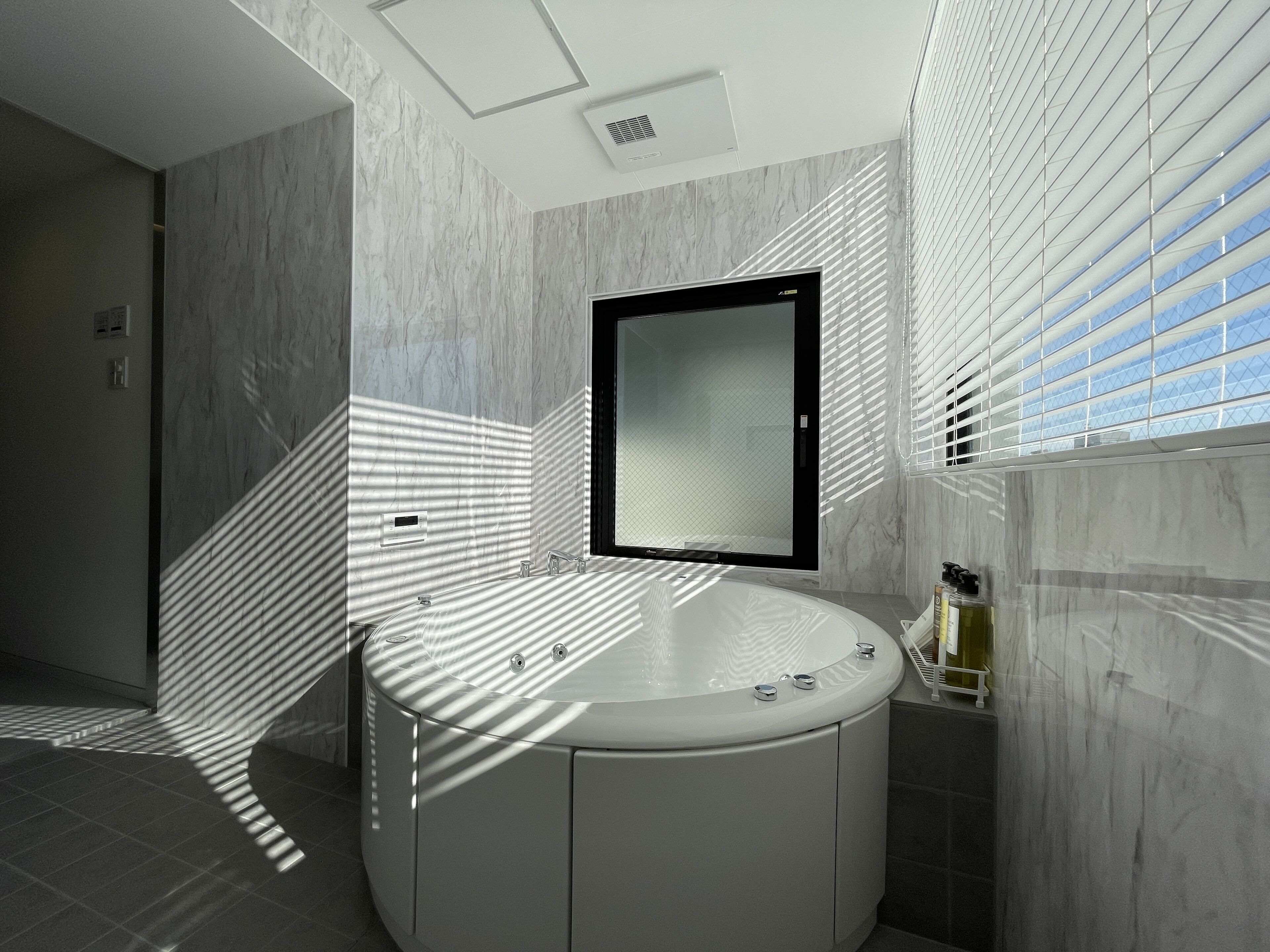 A modern bathroom with a round bathtub, a mirror, and a window with blinds.