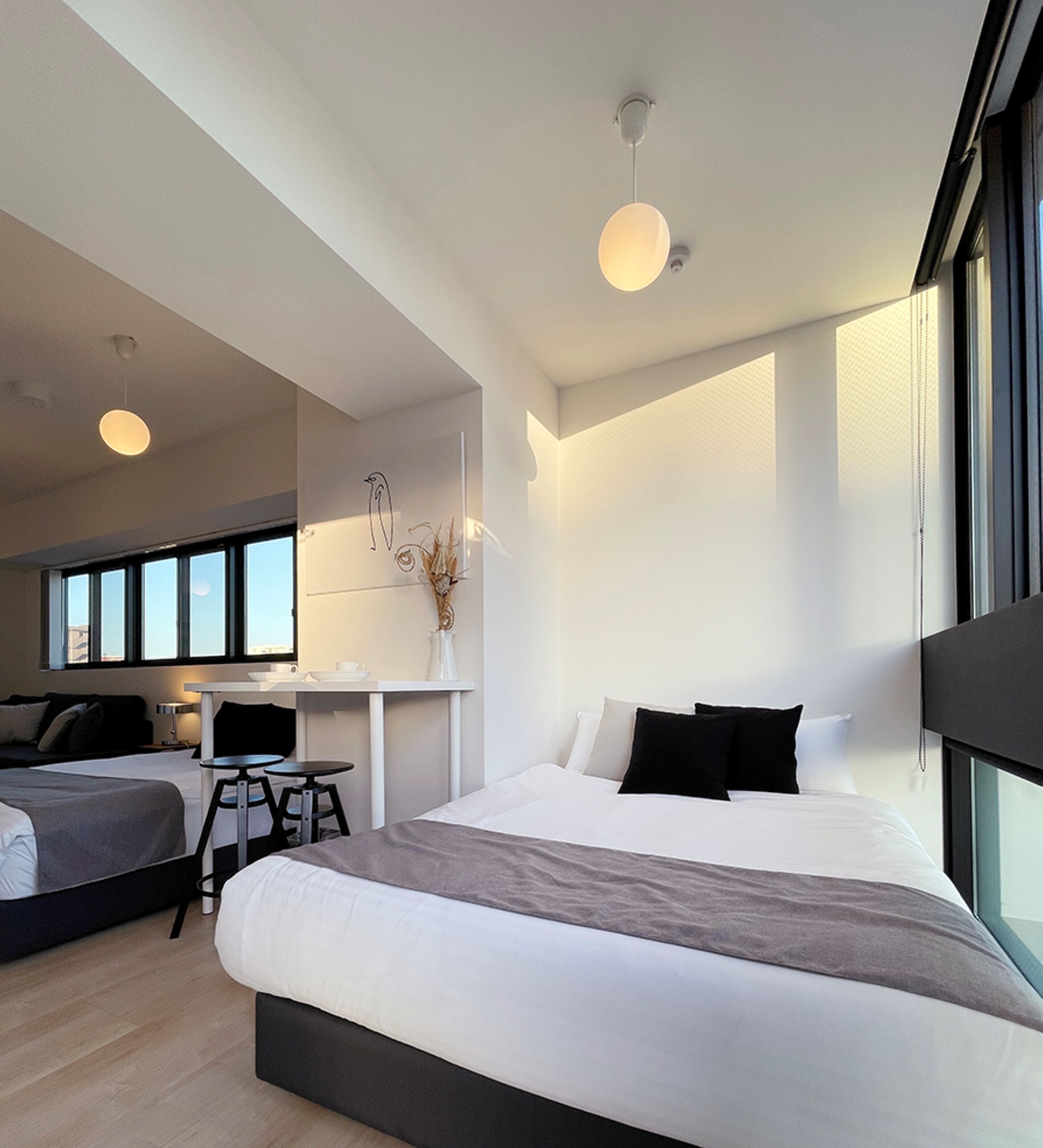 A modern hotel room with a large bed, a desk, and a chair. There is a window providing a view of the city.