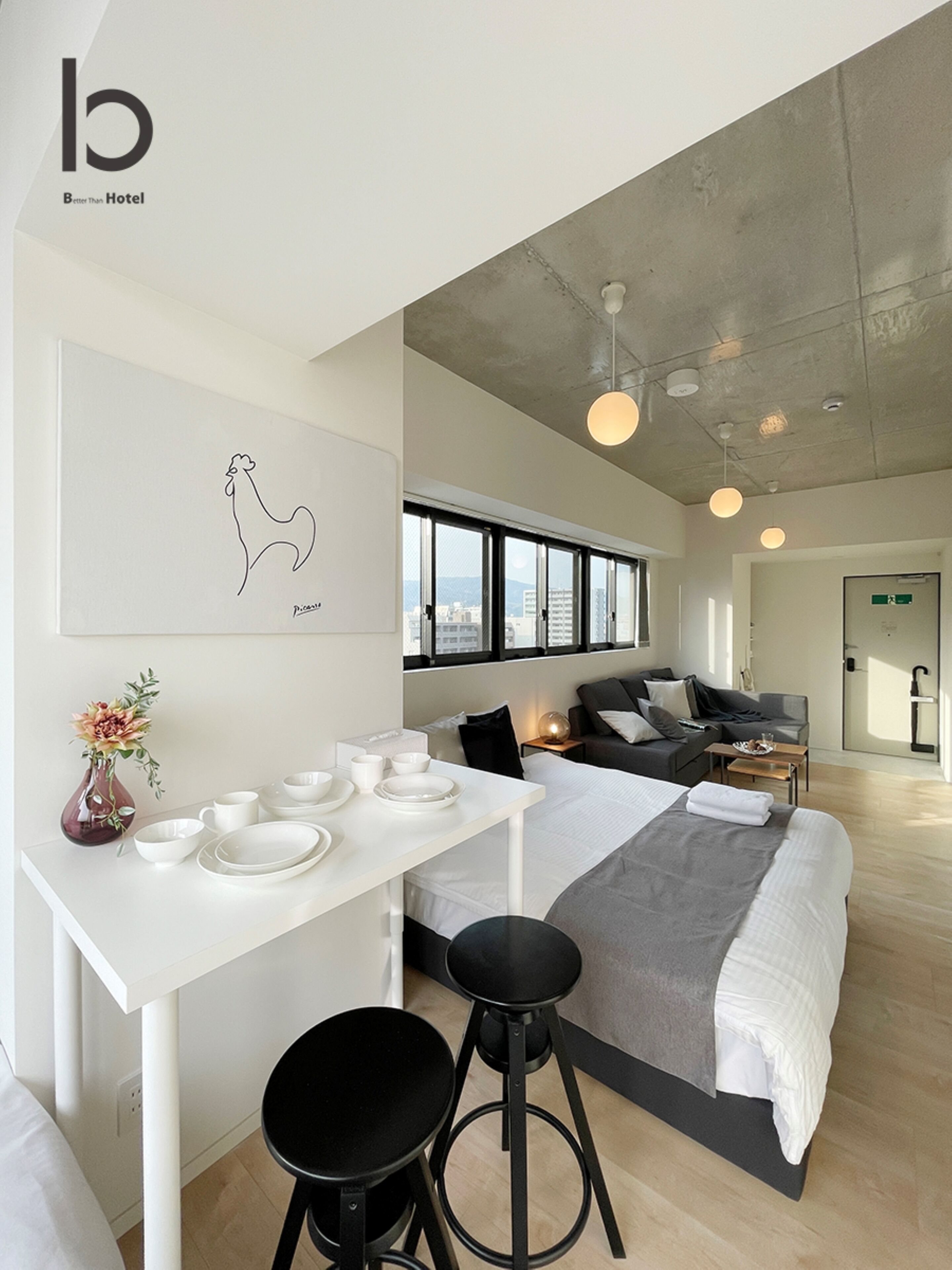 A modern hotel room with a large bed, a dining area with a table set for two, a sofa, and a city view through large windows.